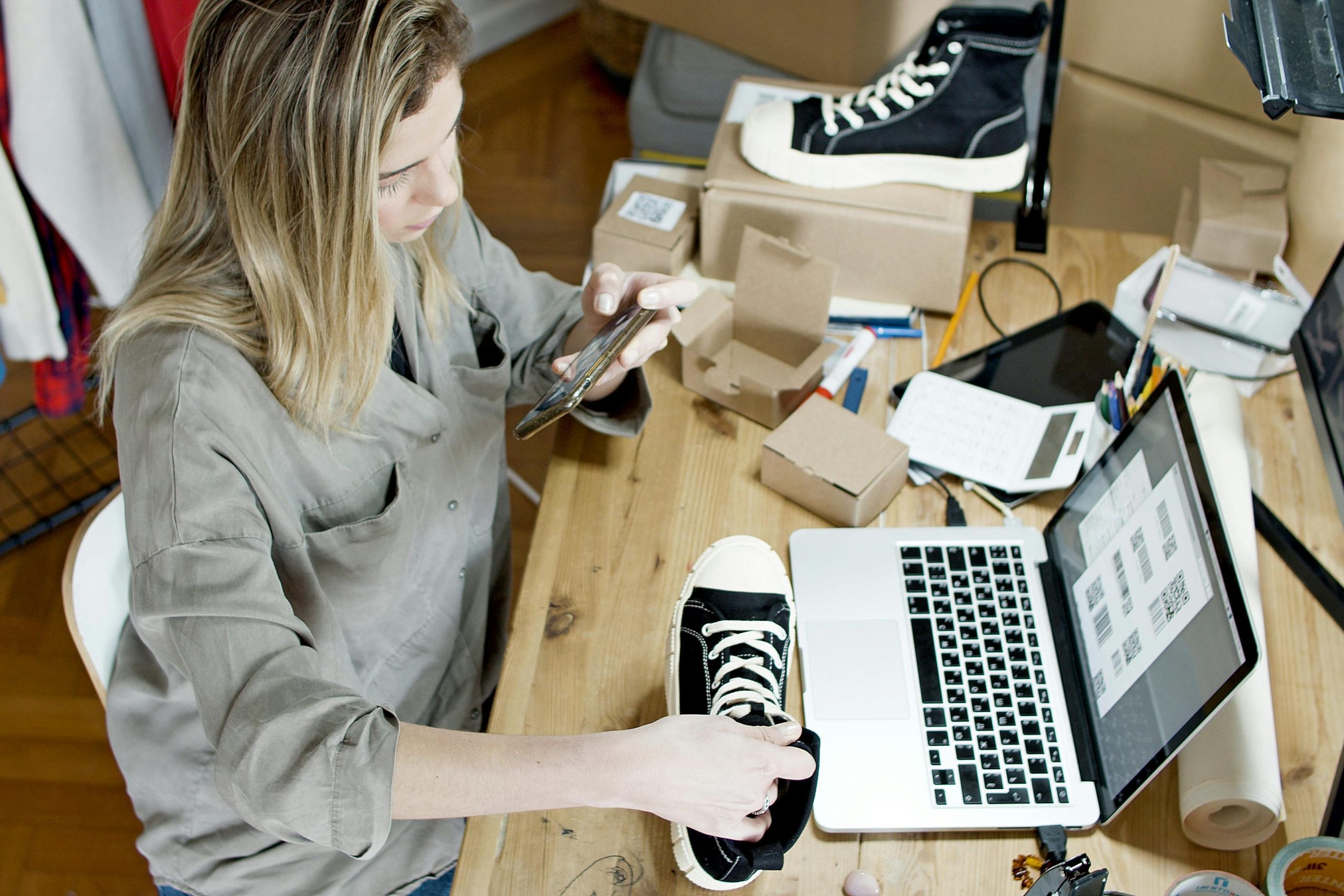online seller taking a photo of a shoe, next to a laptop and cardboard boxes